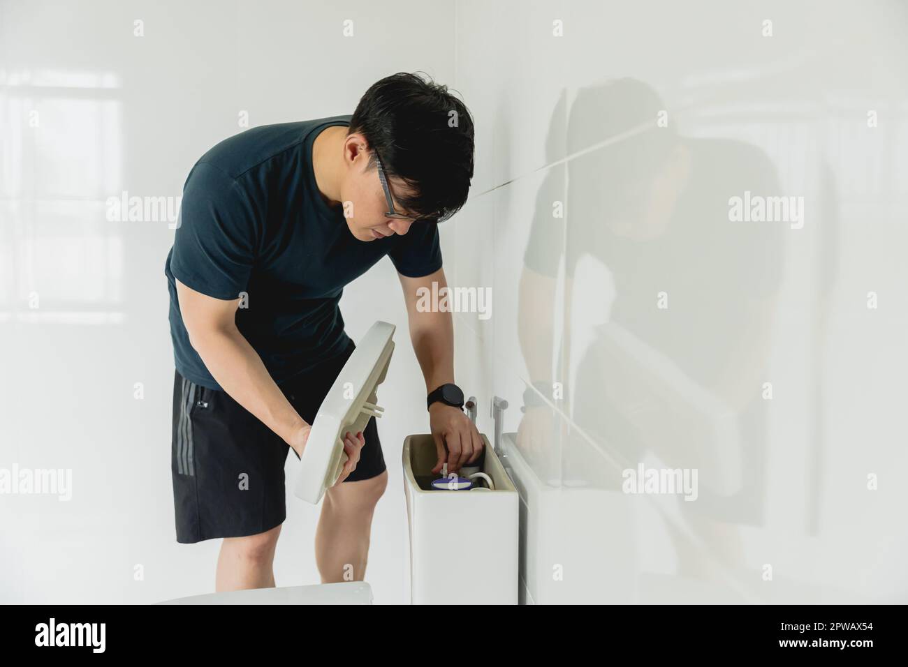 Der Mann, der Hausaufgaben macht, sei ein Handwerker, der den Toilettentank im Badezimmer repariert Stockfoto