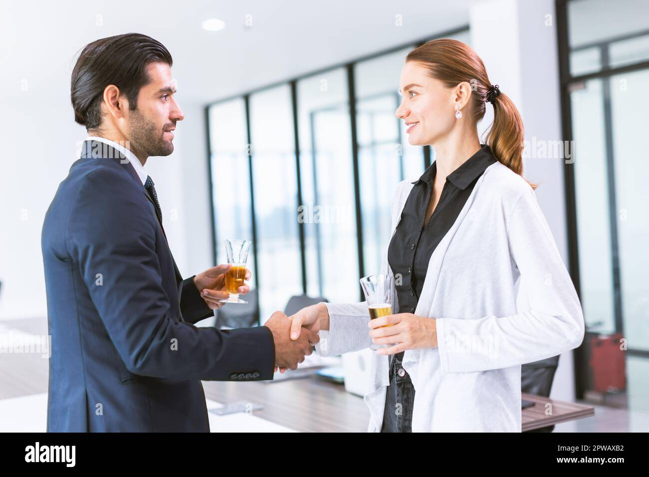 Geschäftsleute treffen sich und führen Händeschütteln bei Alkoholgetränken auf einer Büroparty ein Stockfoto
