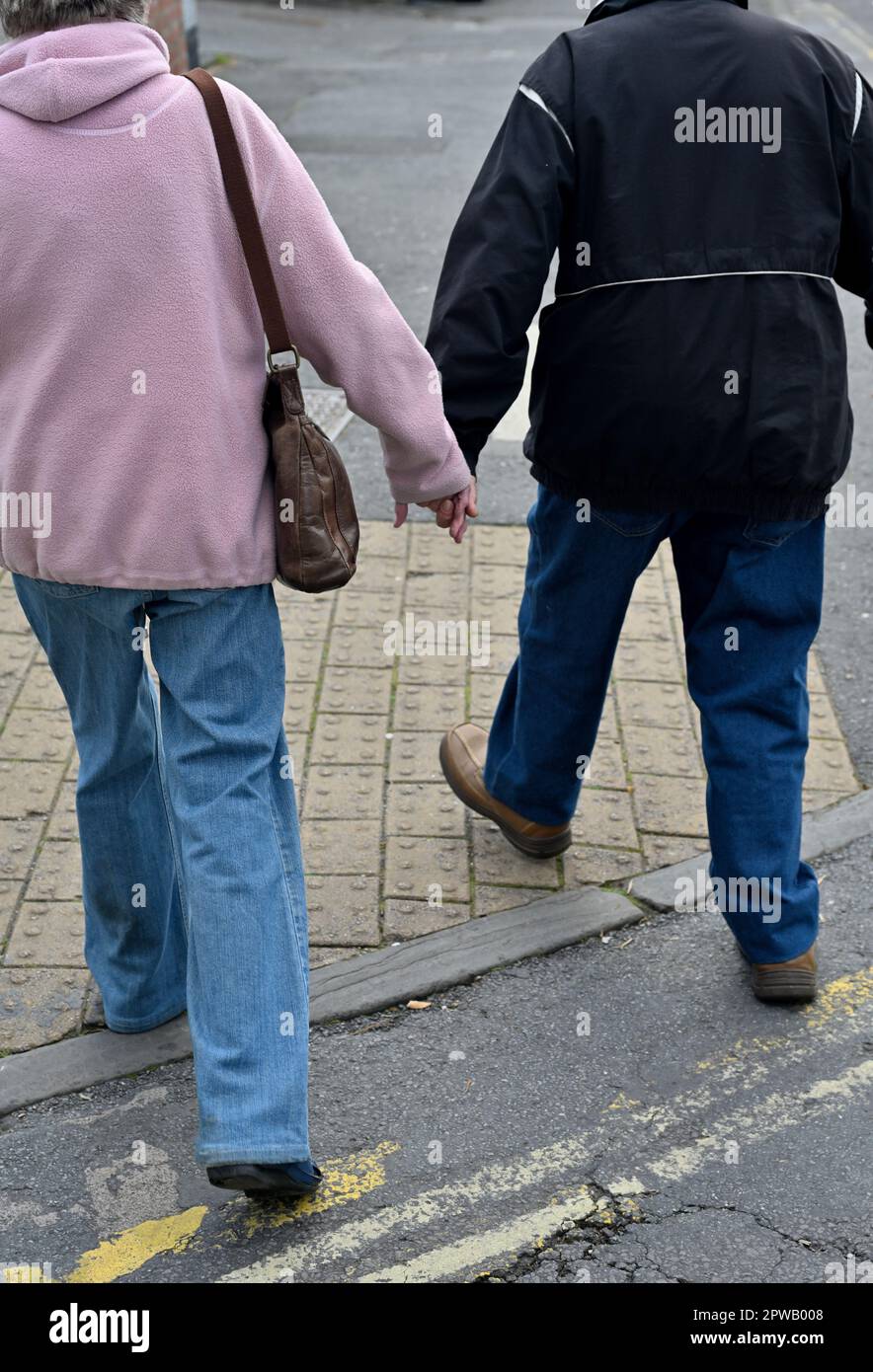 Ein älteres Paar, das auf der Straße wegläuft, auf dem Bürgersteig, Händchen hält Stockfoto