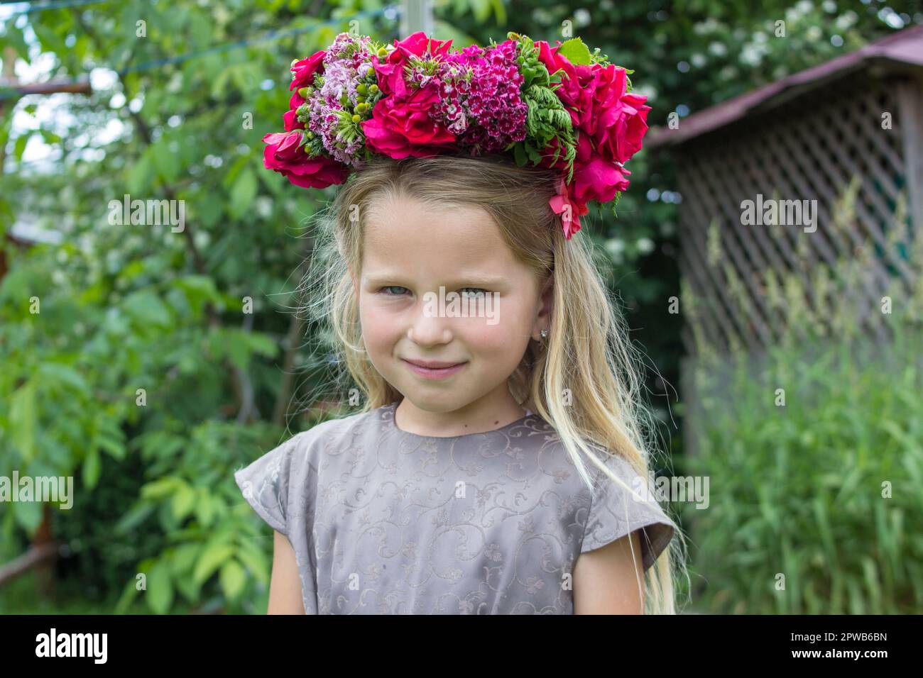 Süßes lächelndes kleines Mädchen mit Blumenkranz auf der Wiese auf der Farm. Porträt eines niedlichen kleinen Kindes im Freien. Mittsommer Stockfoto