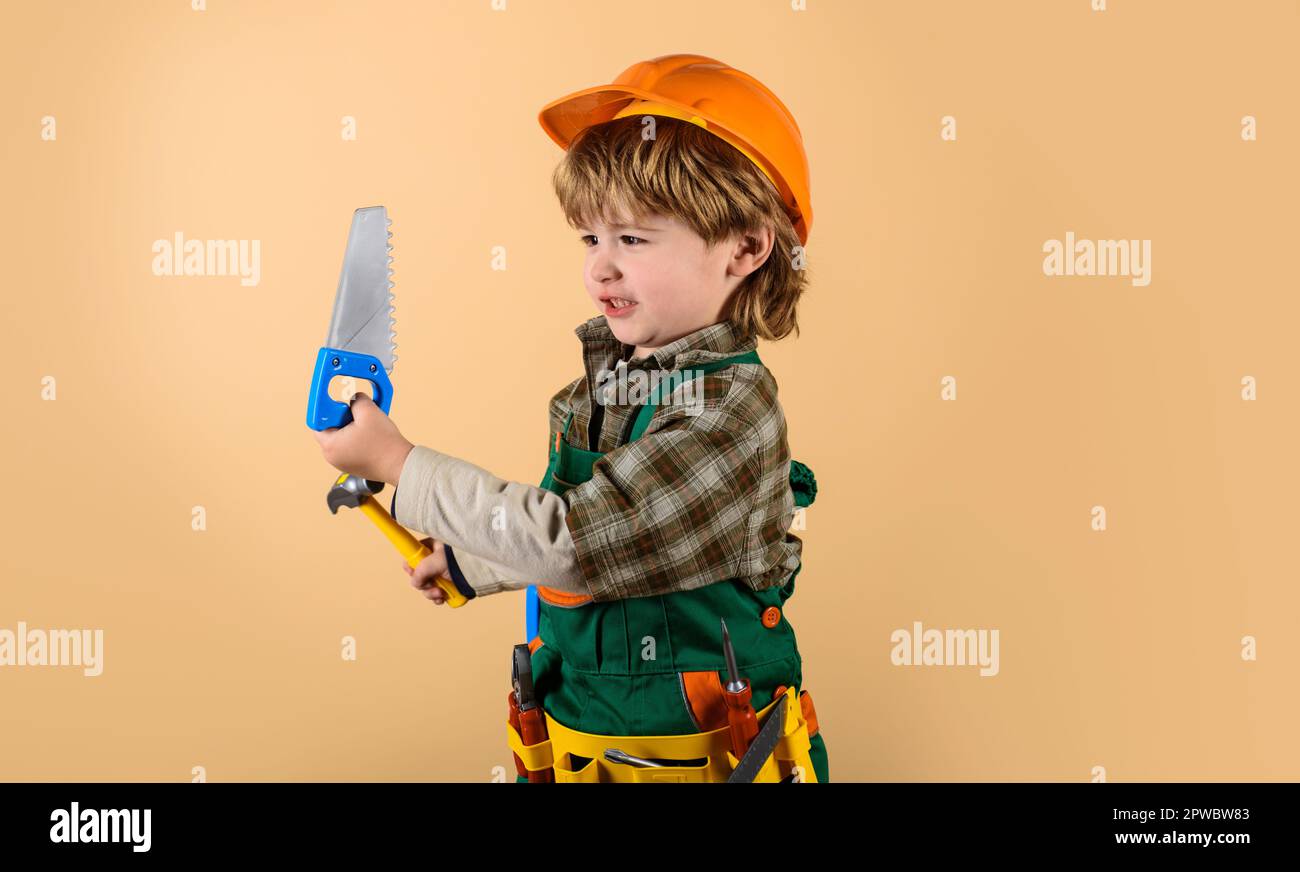 Kleiner Mechaniker mit Säge und Hammer. Kindermechaniker spielt mit Spielzeugwerkzeugen, die repariert werden sollen. Kleiner Baumeister mit Werkzeuggürtel. Ein Junge in Baumeister-Uniform Stockfoto