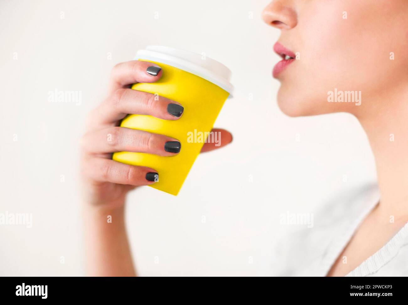Crop anonyme Frau in warmen Pullover mit dunkelgrauen Maniküre Halten Einweg-Tasse Kaffee, während sich auf Holztisch Stockfoto