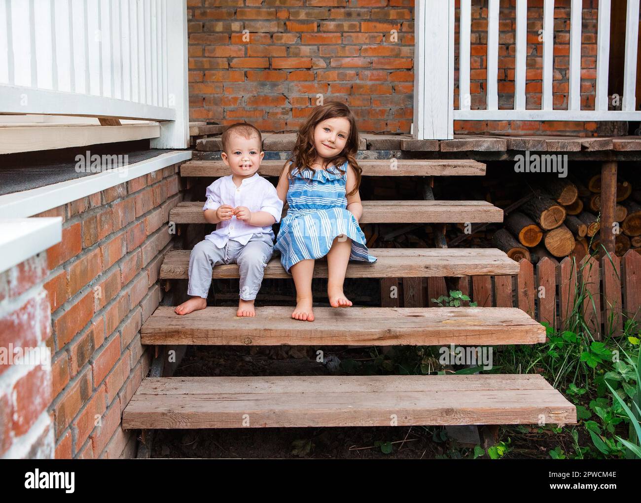 Nette kleine Bruder und Schwester sitzen auf Holztreppe in der Nähe der Veranda des Landhauses und entspannen in ländlicher Umgebung während der Sommerferien Stockfoto