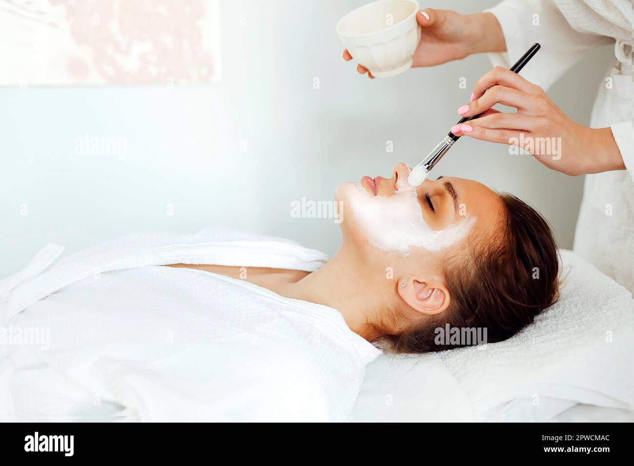 Unkenntlich weibliche Kosmetikerin Anwendung Tonmaske mit Pinsel auf Gesicht Der entspannten Client während der Hautpflege Verfahren im Spa-Salon Stockfoto