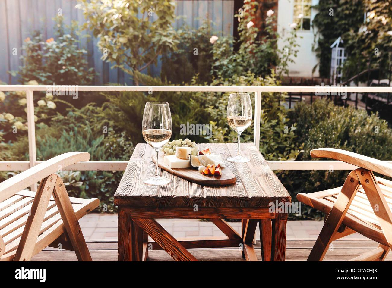 Gläser Wein und Teller mit Obst und Käse auf Holztisch neben Stühlen an sonnigen Sommertagen auf der Terrasse platziert Stockfoto
