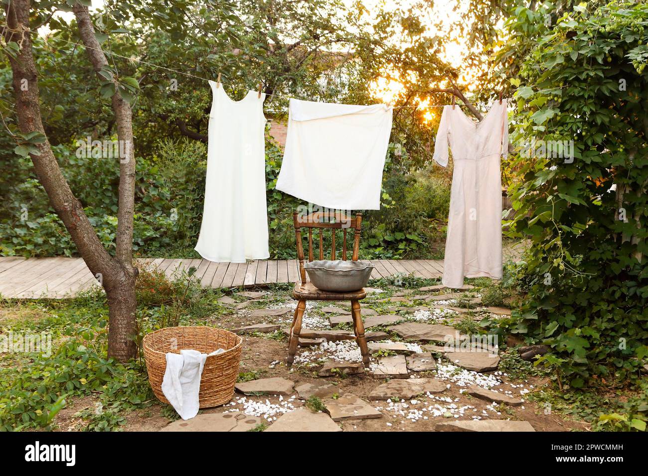 Reinigen Sie nasse Kleidungsstücke, die an einem Seil hängen und trocknen Sie sie am Wäschetag in der Nähe eines Retro-Stuhls und einer Schüssel im Garten Stockfoto
