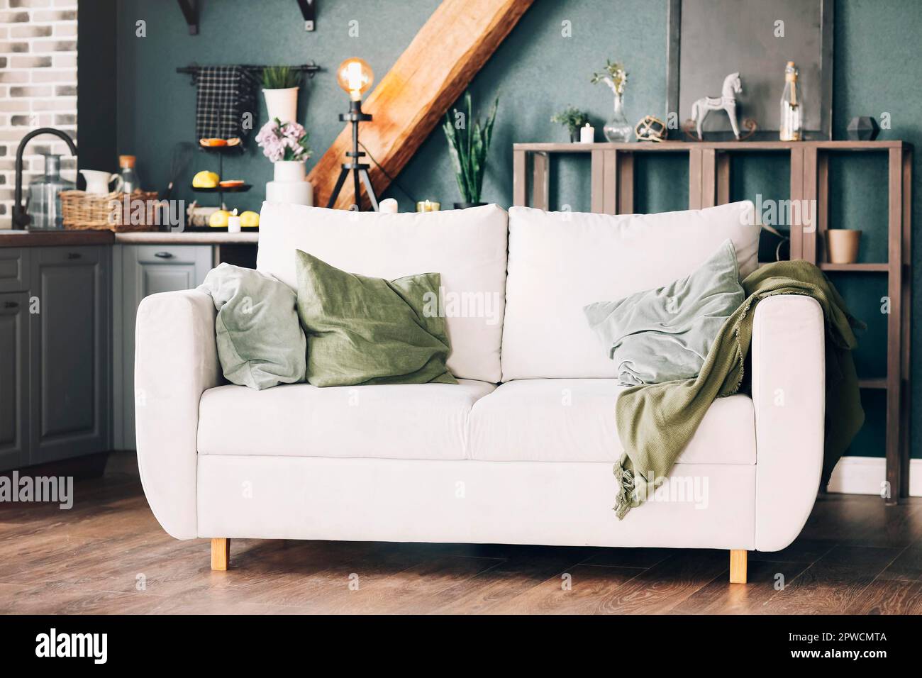 Weißes Sofa mit grünen und grauen Velours-Kissen in amerikanischem Stil, moderne Küche, Holzbücherregal hinter Couch dekoriert mit Stockfoto