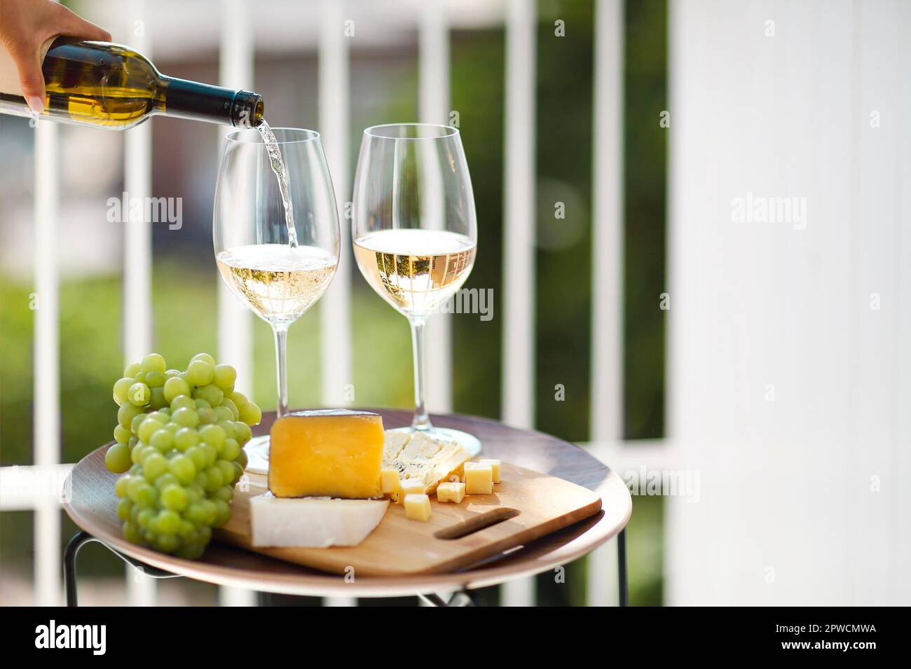 Gläser Wein und Teller mit Obst und Käse auf Holztisch neben Stühlen an sonnigen Sommertagen auf der Terrasse platziert Stockfoto