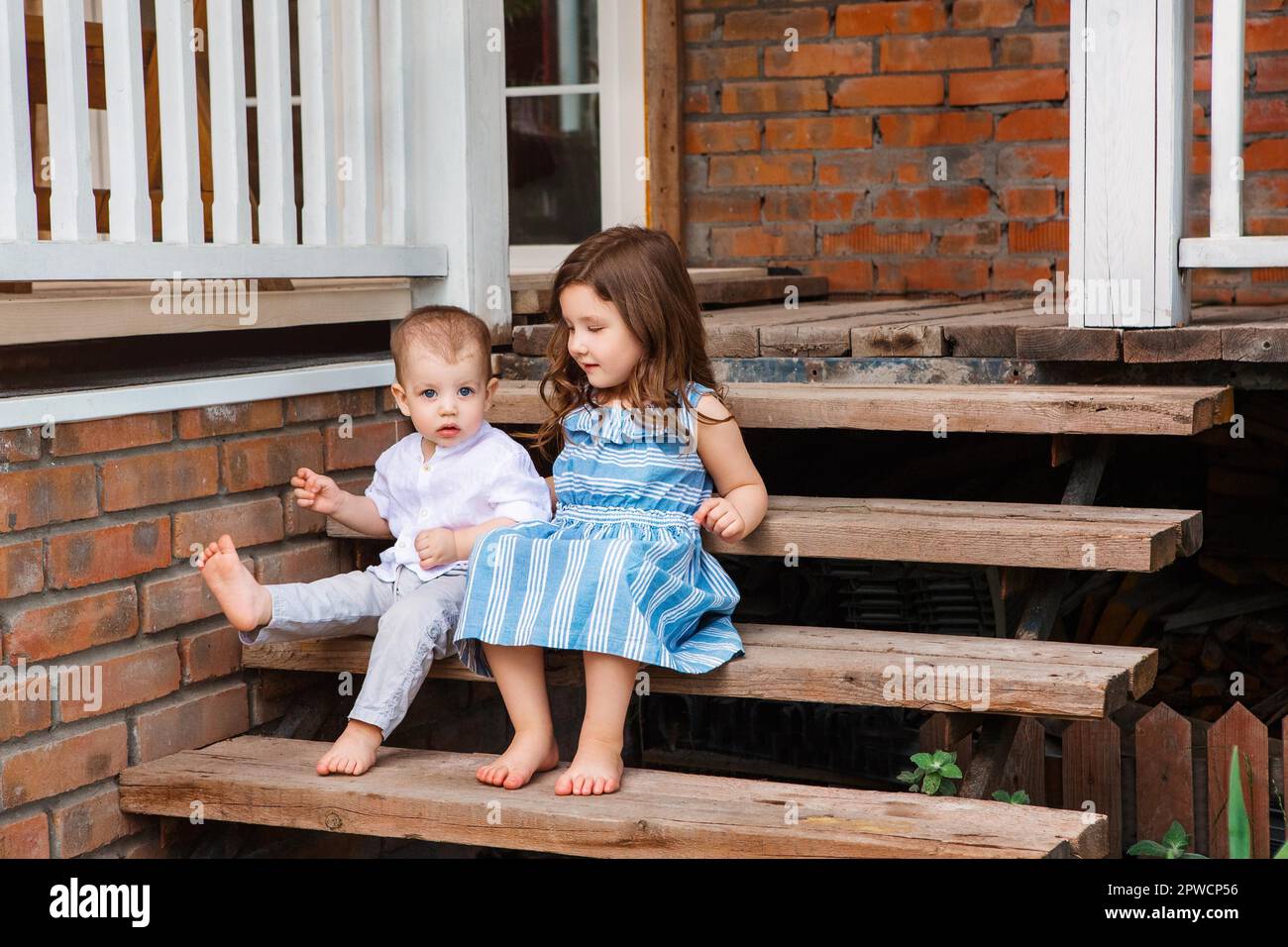 Nette kleine Bruder und Schwester sitzen auf Holztreppe in der Nähe der Veranda des Landhauses und entspannen in ländlicher Umgebung während der Sommerferien Stockfoto