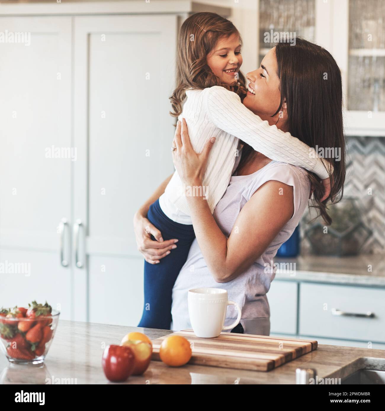 Ihr Lieblingsplatz ist in Müttern Umarmung. Eine glückliche Mutter, die ihr süßes kleines Mädchen in der Küche zu Hause umarmt. Stockfoto