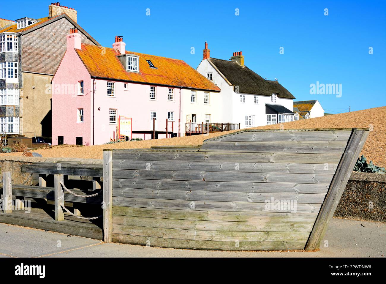 Sitzbereich in Holzbootform entlang des Kais mit hübschen Strandhäuschen hinten, West Bay, Dorset, Großbritannien. Stockfoto