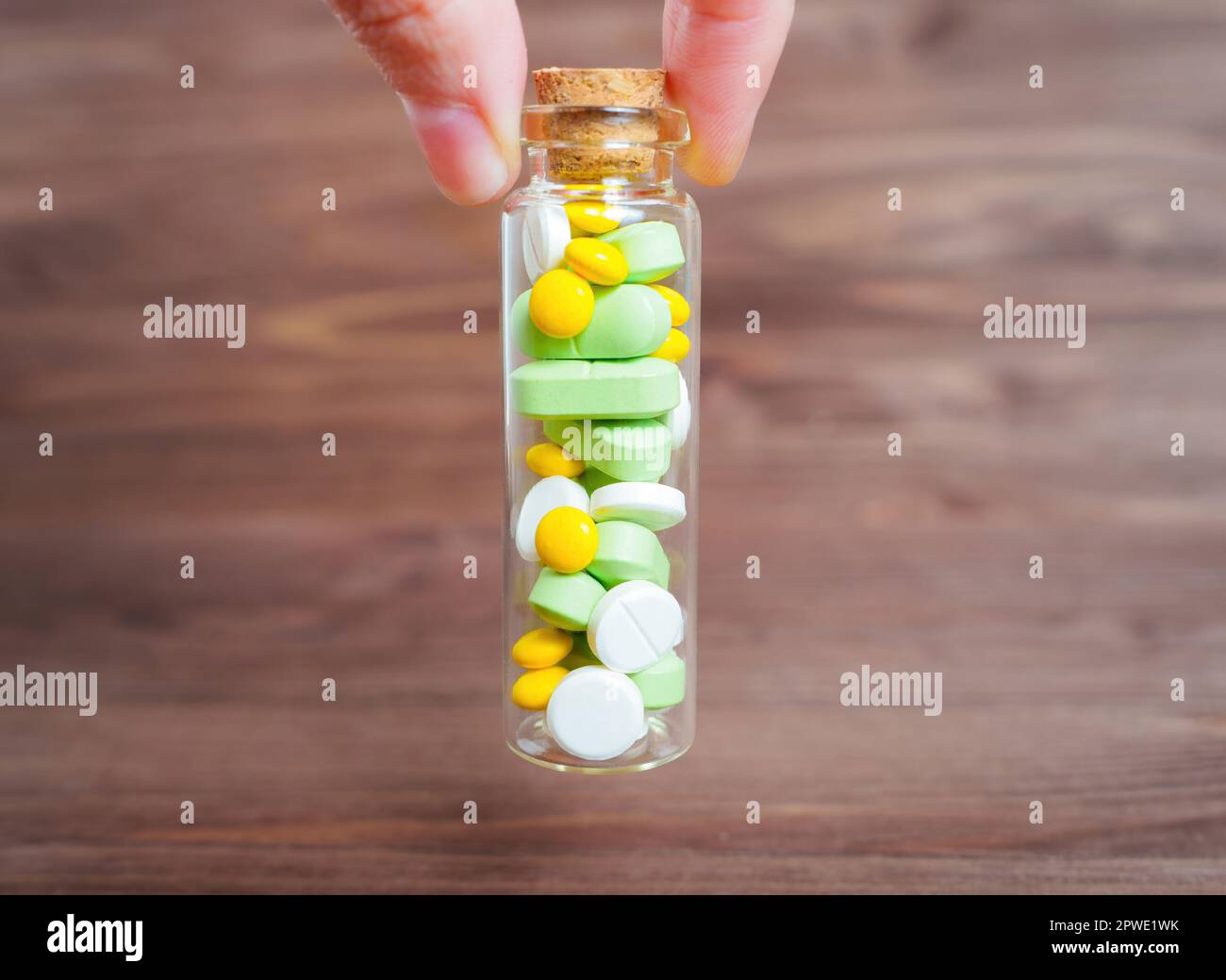 Halten Sie eine kleine Flasche aus Glas mit ovalen und runden grünen, gelben und weißen Pillen vor einem dunklen Holztisch. Medikamentenmann Stockfoto