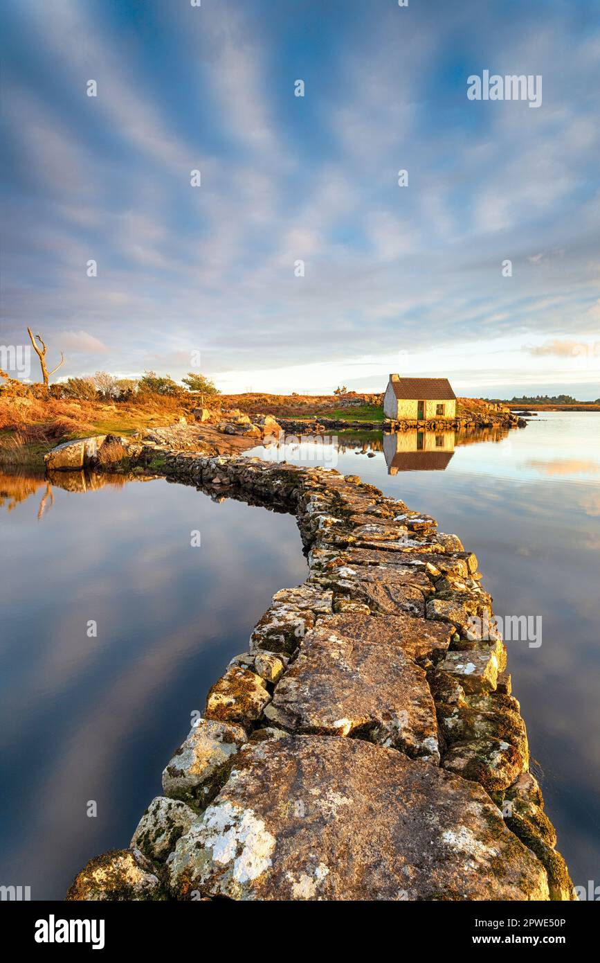 Ein alter Steinsteg über einen See, der zu einem kleinen Häuschen im Connemara-Nationalpark in Irland führt Stockfoto