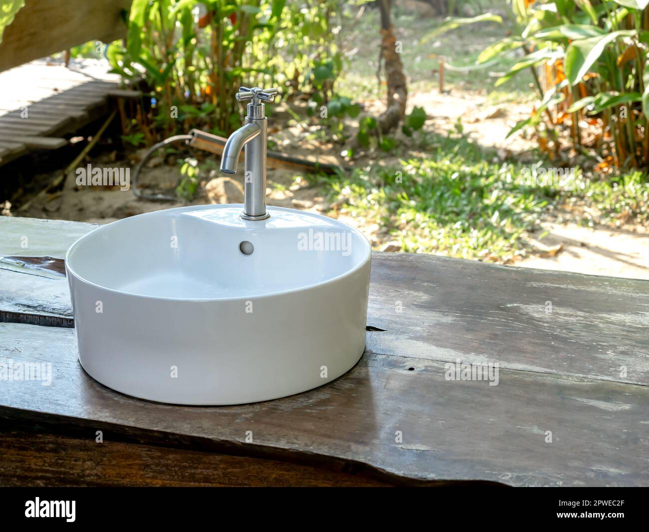 Matt verchromter Wasserhahn auf rundem Keramikbecken Spülbecken auf Holztisch Gartenhintergrund mit Kopierbereich. Modernes Design mit natürlichem Bad Stockfoto
