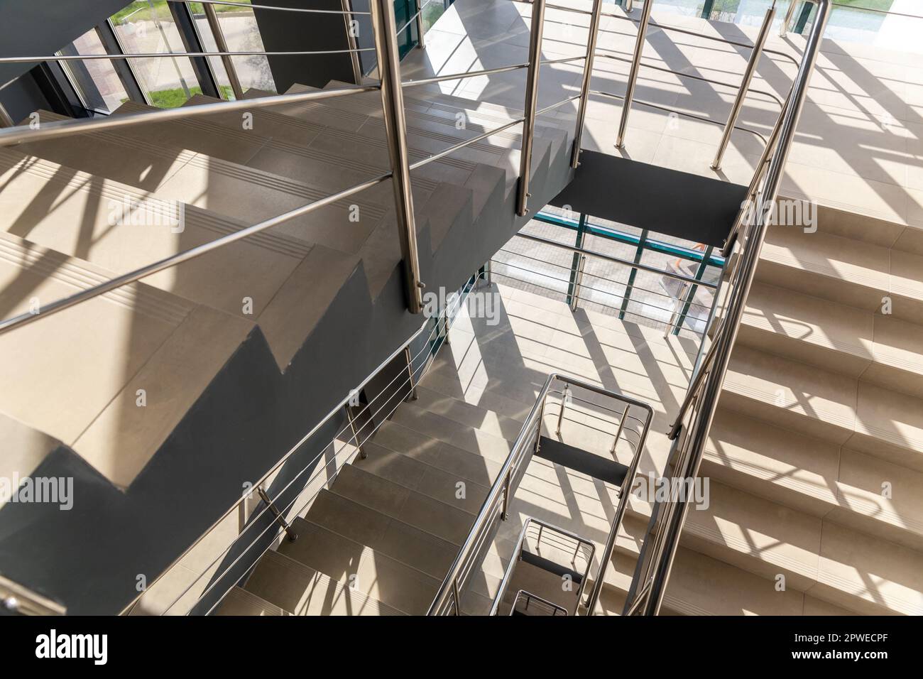 Treppen in einem Betonbürogebäude in neutralen Farbtönen, mit Keramikfliesen bedeckt, mit glänzenden Metallgeländern aus Edelstahl, extensivem Glaszin Stockfoto
