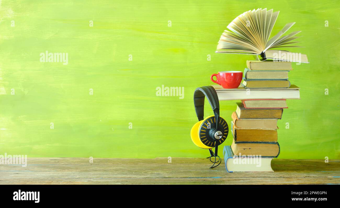 Hörbuchkonzept mit Bücherstapel, eines geöffnet, Kaffeetasse und Oldtimer-Kopfhörer, Panoramablick, kostenloser Kopierbereich Stockfoto