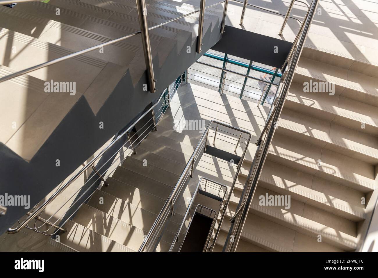Treppen in einem Betonbürogebäude in neutralen Farbtönen, mit Keramikfliesen bedeckt, mit glänzenden Metallgeländern aus Edelstahl, extensivem Glaszin Stockfoto