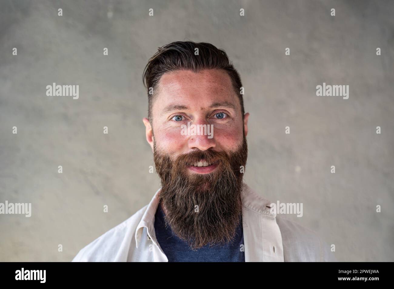 Portrait eines glücklichen Hipsters aus nordeuropa - selbstbewusster und lächelnder bärtiger Mann mit eigenartigen blauen Augen, der Spaß hat, während er vor den Reisenden posiert Stockfoto