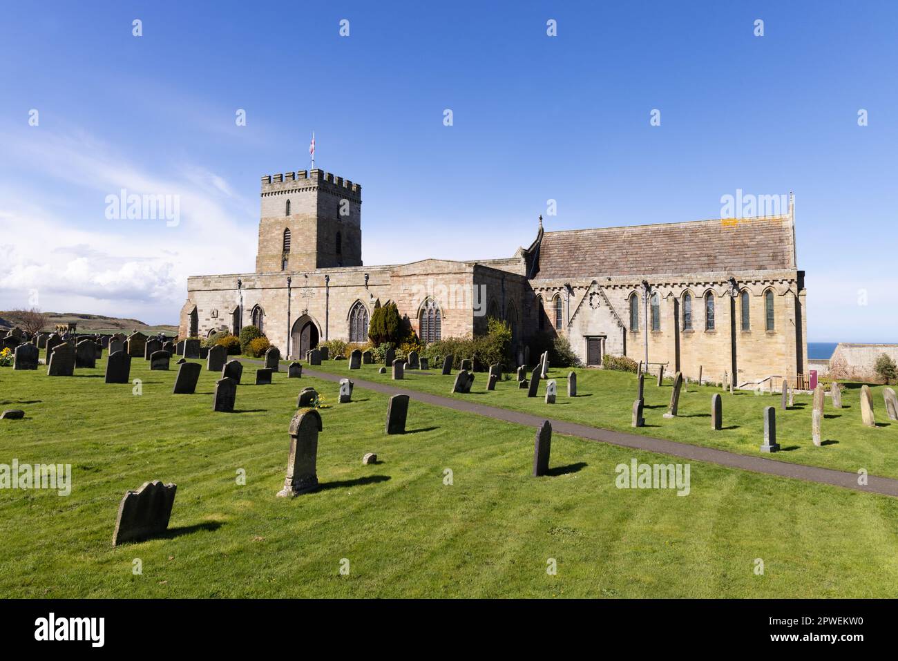 St Aidans Church Bamburgh Northumberland UK; Außenansicht an einem sonnigen Frühlingstag mit blauem Himmel. Das Grab von Grace Darling ist ganz links zu sehen. Stockfoto