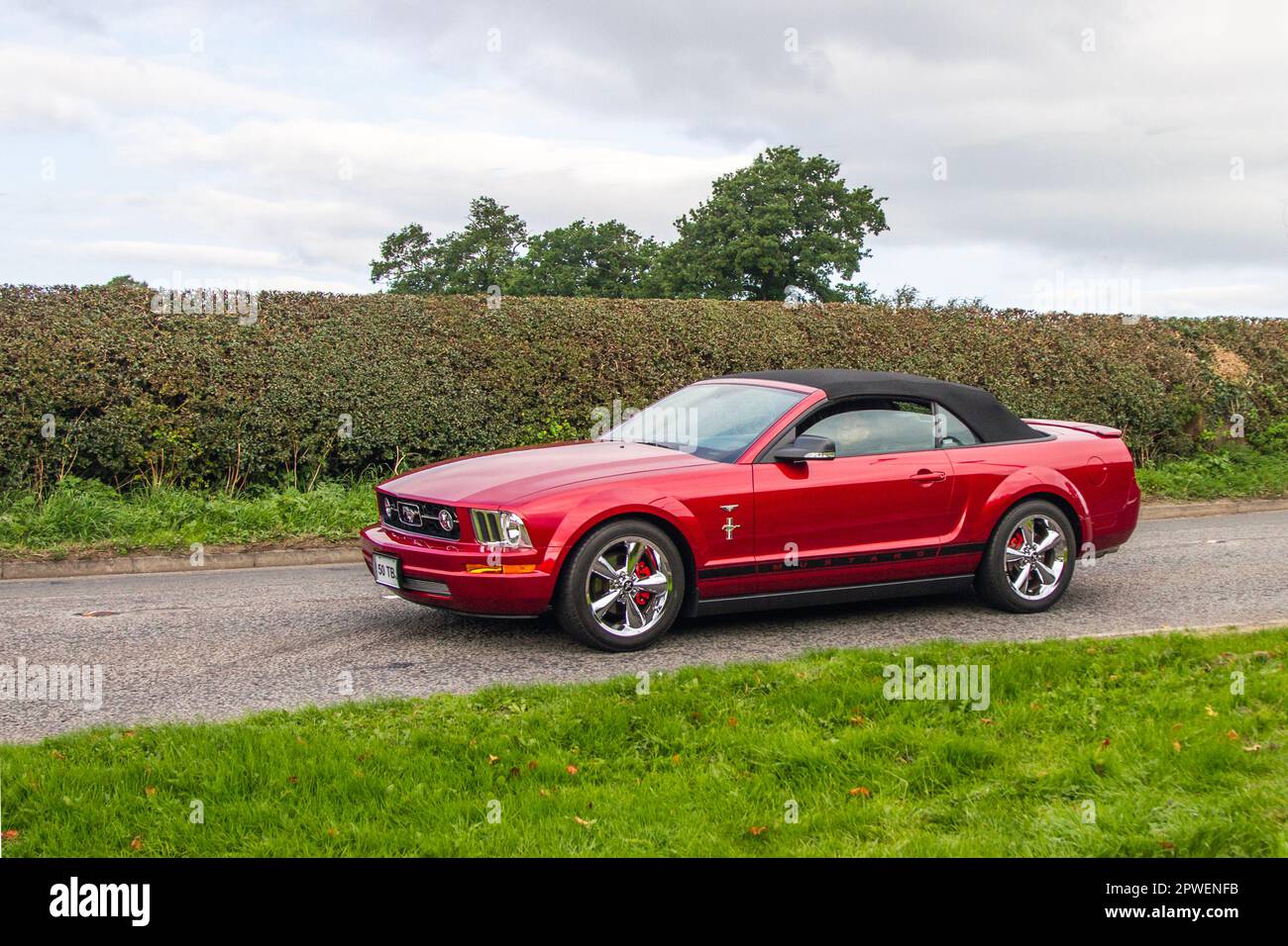 2007 Red Ford Mustang 4000 cc Cabrio; isolierter Oldtimer auf einer Landstraße in Congleton, Großbritannien Stockfoto