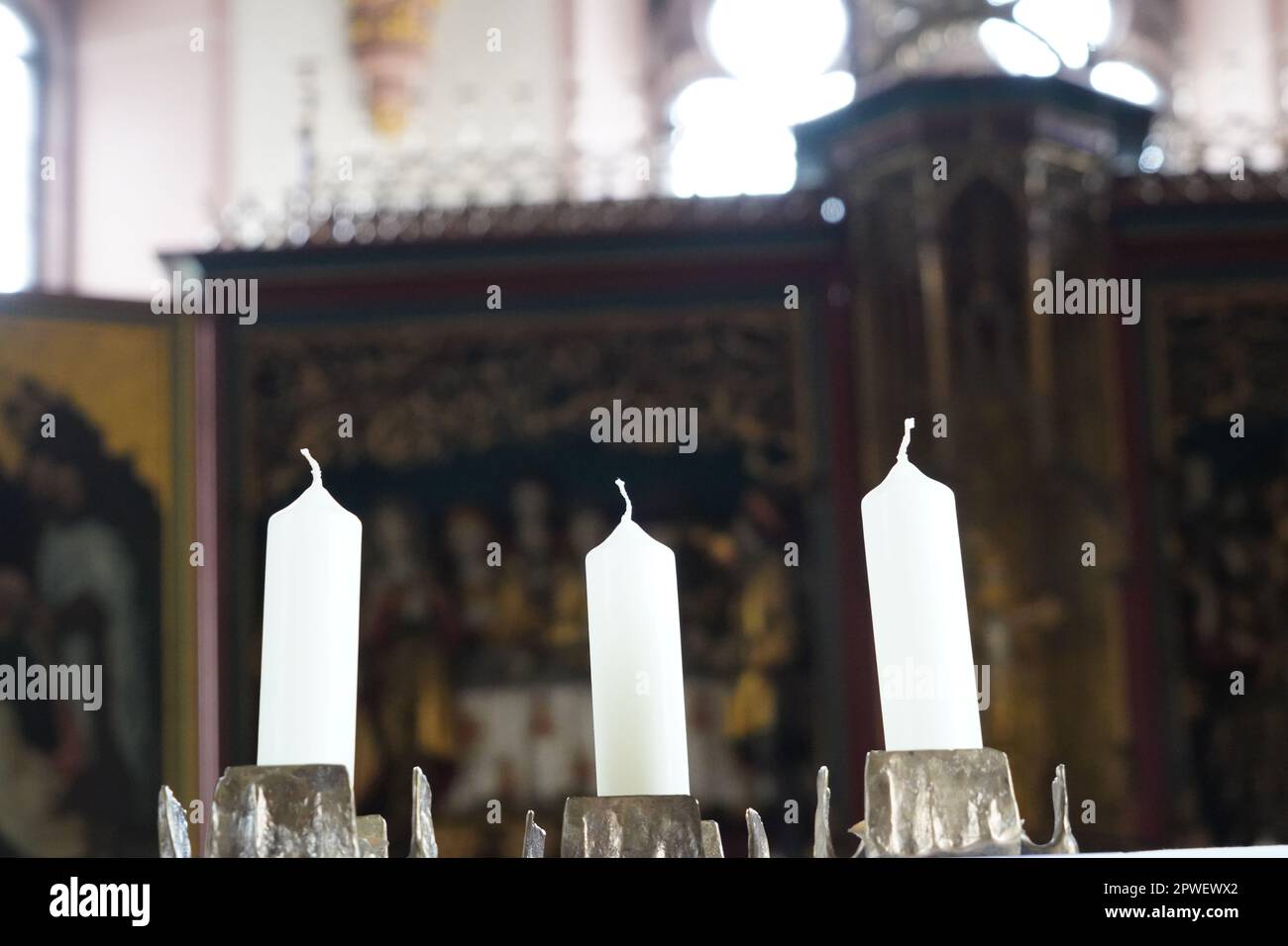Drei weiße Kerzen in einem Kronleuchter in einer Kirche. Im Hintergrund ist ein unscharfer Altar. Stockfoto