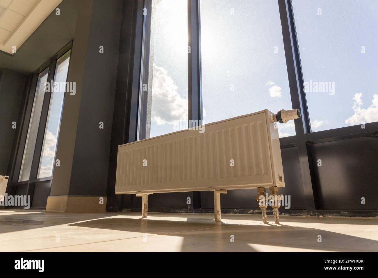 Vertikal installierter Zentralheizungskühler auf dem Boden an der vollständig verglasten Außenwand des Bürogebäudes. Ein weißer Heizkörper in einem Raum mit einem Stockfoto