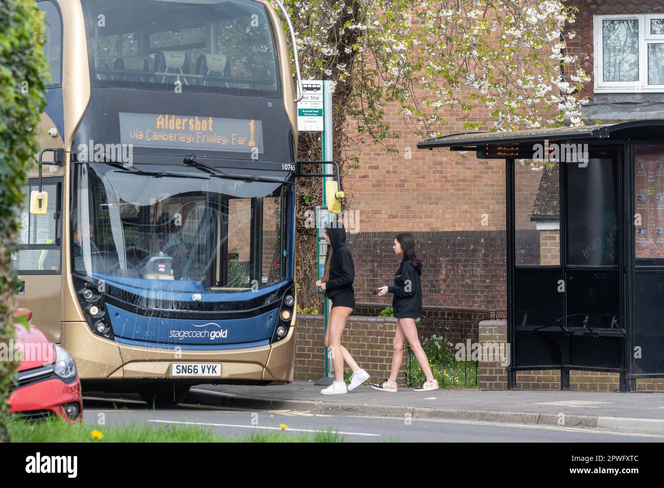 Zwei Mädchen im Teenageralter in Shorts, die an einer Bushaltestelle in Surrey, England, in einen Bus einsteigen. Öffentliche Verkehrsmittel, Alltag, 2023 Stockfoto