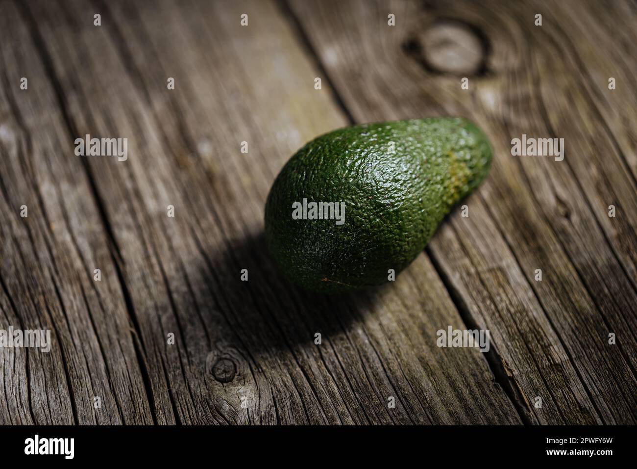 Eine Avocado-Frucht auf einem rustikalen Holztisch und dramatische Stimmung. Aktienfoto Stockfoto