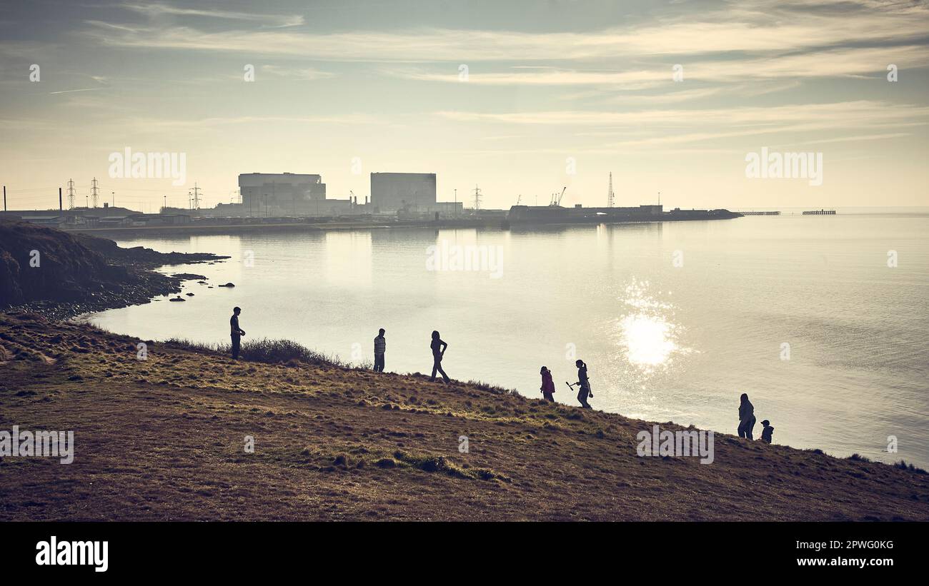 Eine Gruppe junger Leute in einer Silhouette gegen das Kernkraftwerk in Heysham, Lancashire, Großbritannien Stockfoto