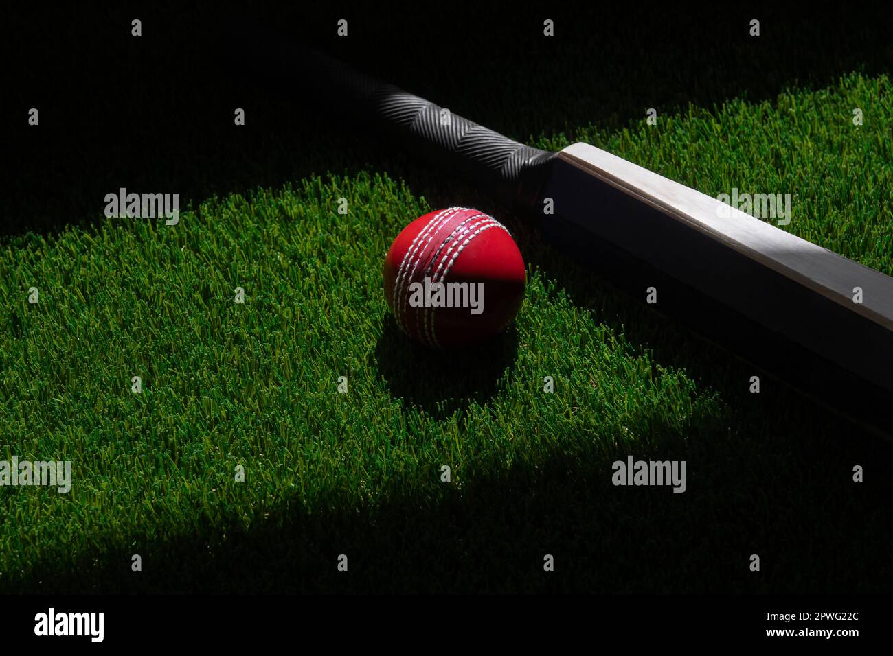 Cricketschläger und roter Ball mit natürlichem Licht auf grünem Gras. Horizontales Sportposter, Grußkarten, Kopfzeilen, Website und App Stockfoto