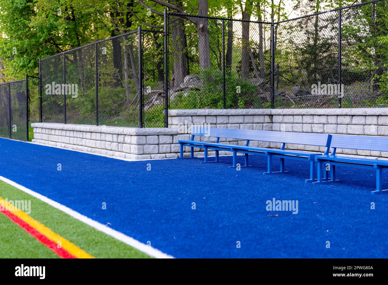 Am späten Nachmittag Foto eines blauen Sitzes oder einer Bank mit Kunstrasenfeld und Haltewand im Hintergrund. Stockfoto