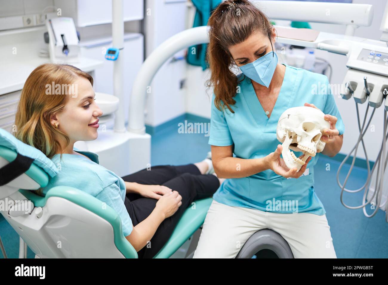 Von oben weibliche Zahnärztin in Uniform und Gesichtsmaske, die den menschlichen Schädel zeigt