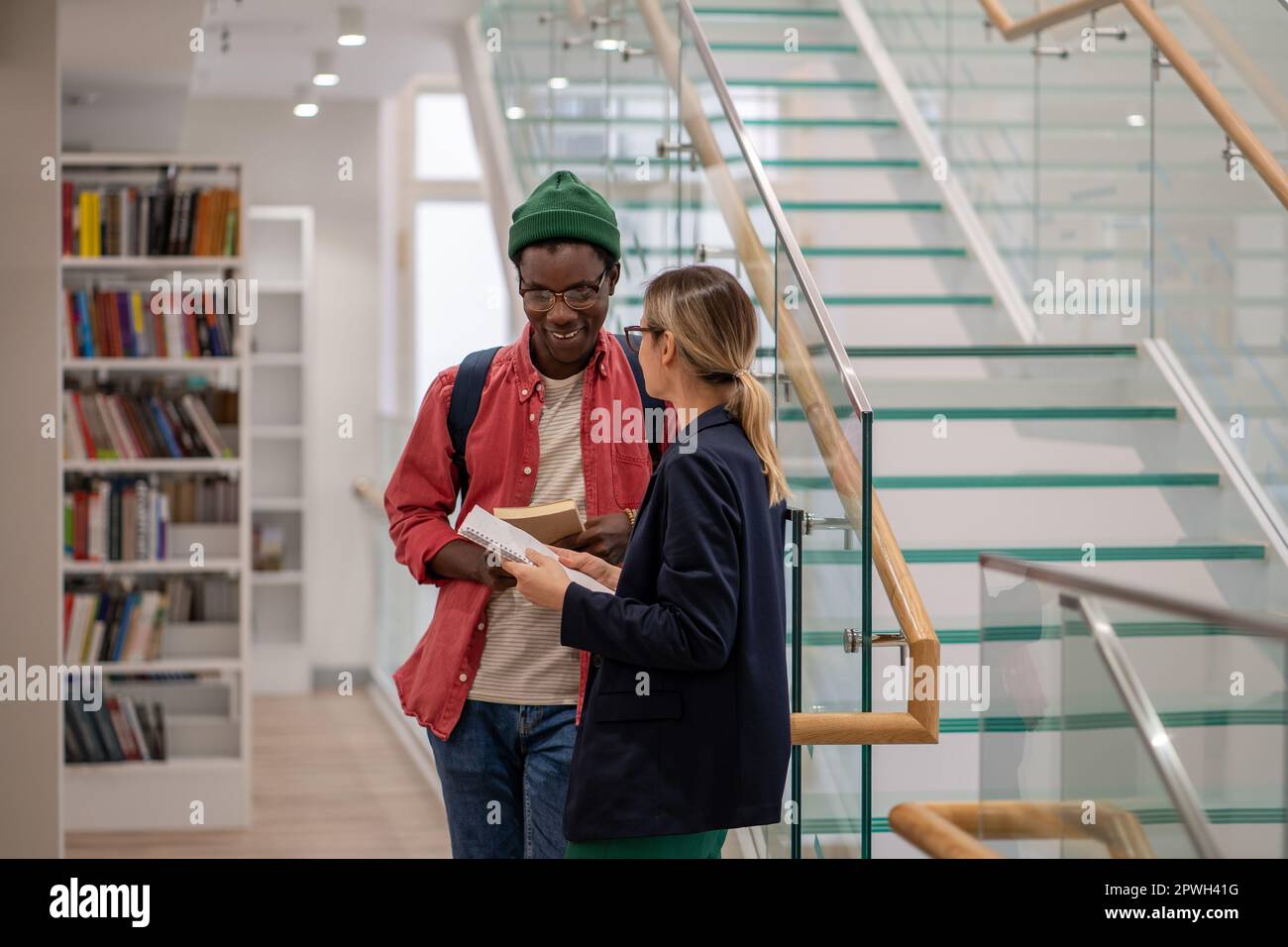 Lächelnde afroamerikanische Studentenkommunikation mit europäischer Freundin in der Universitätsbibliothek Stockfoto