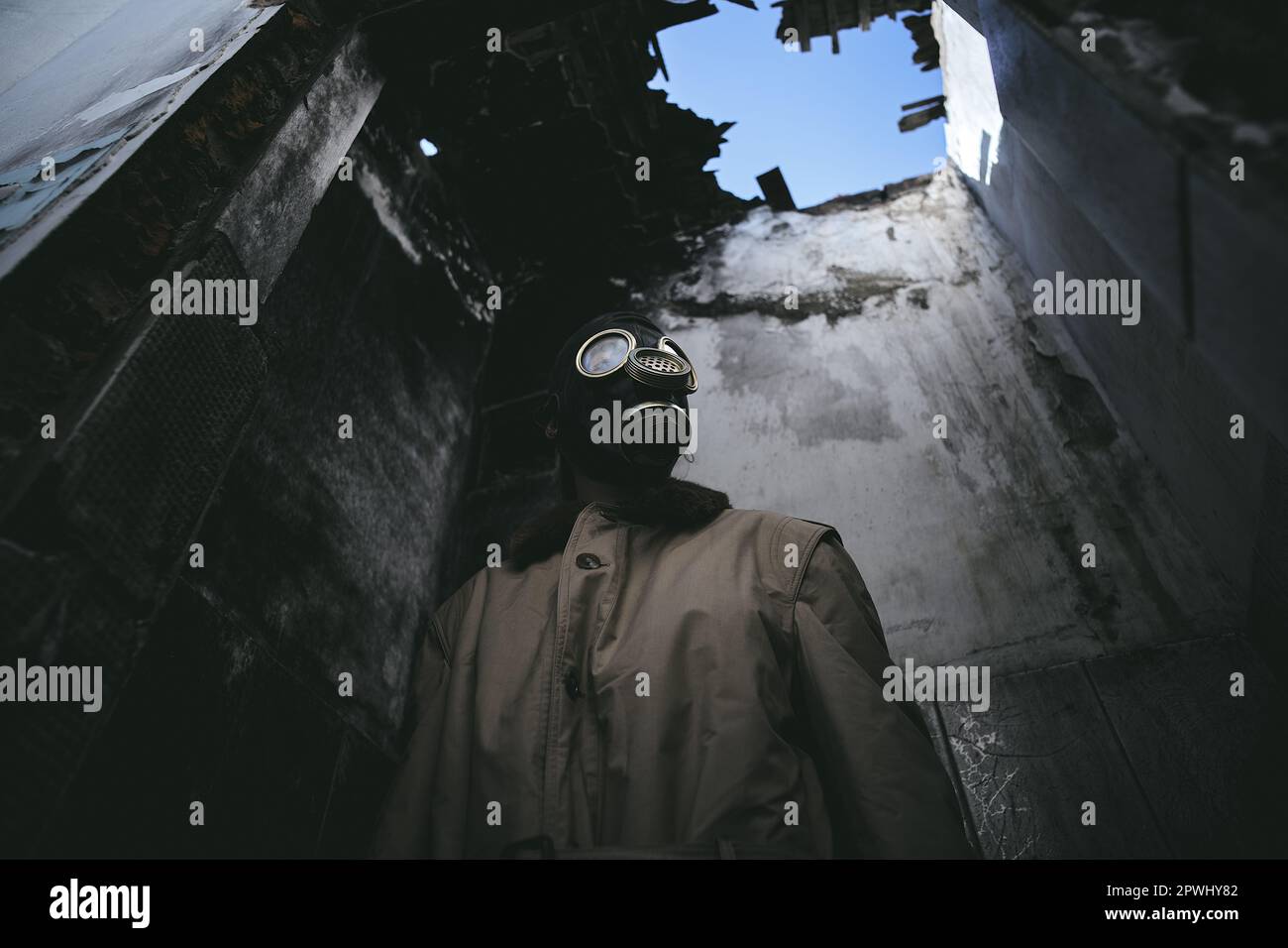 Ein Mann, der eine Gasmaske in einem zerstörten Gebäude trägt, mit einem undichten Dach im Dunkeln, Apokalypse, gut für den Bucheinband, niedriger Winkel Stockfoto