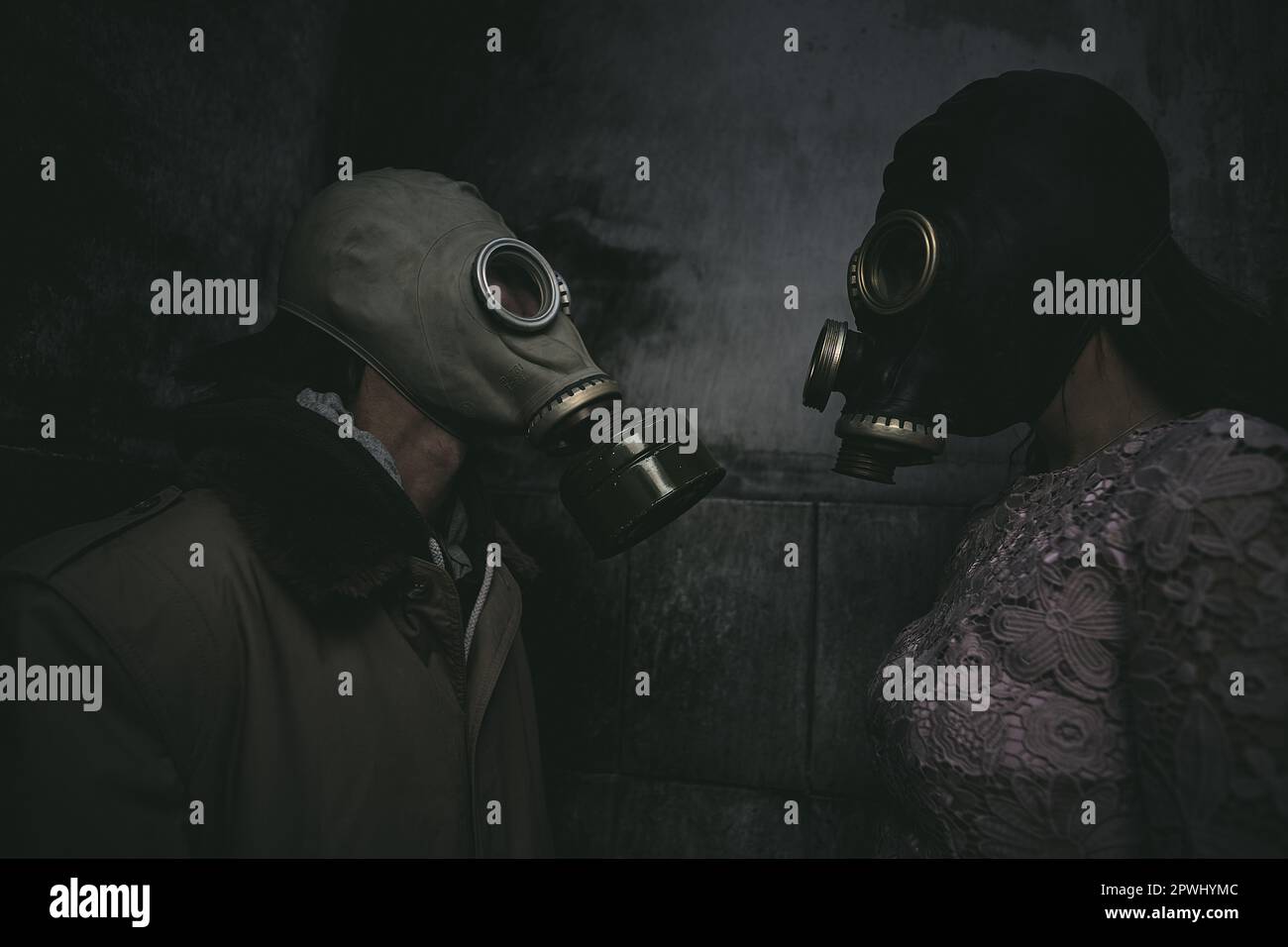 Zwei Personen mit Gasmasken stehen in einem kleinen dunklen Raum an einer Wand und schauen einander an, Nahaufnahme, gut für den Bucheinband Stockfoto