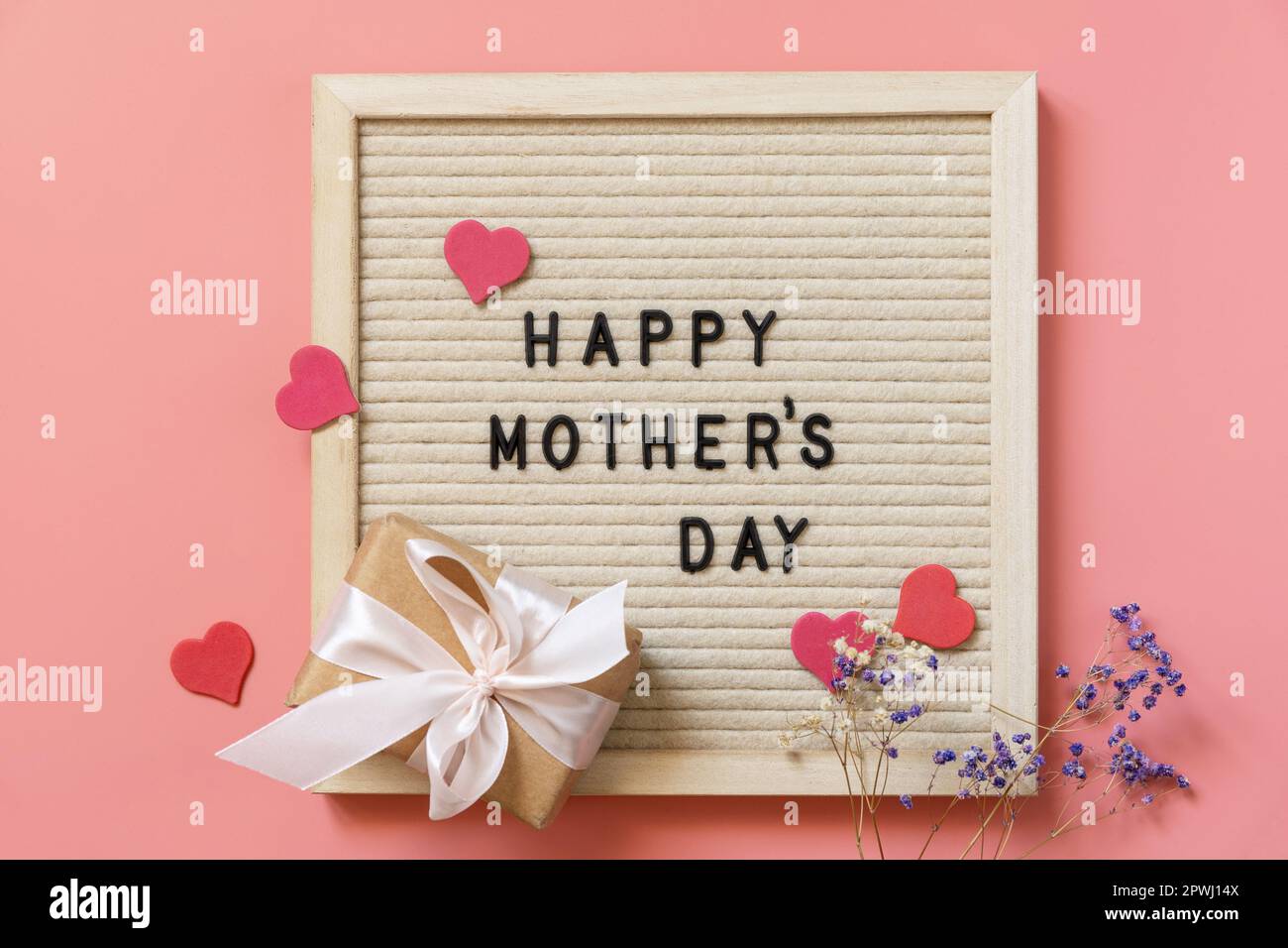 Geschenkbox mit Schleifen kleine Herzen und Zigeunerblüten auf pastellrosa Hintergrund mit leerem Platz. Muttertagsfeier-Konzept. Blick von oben. Stockfoto