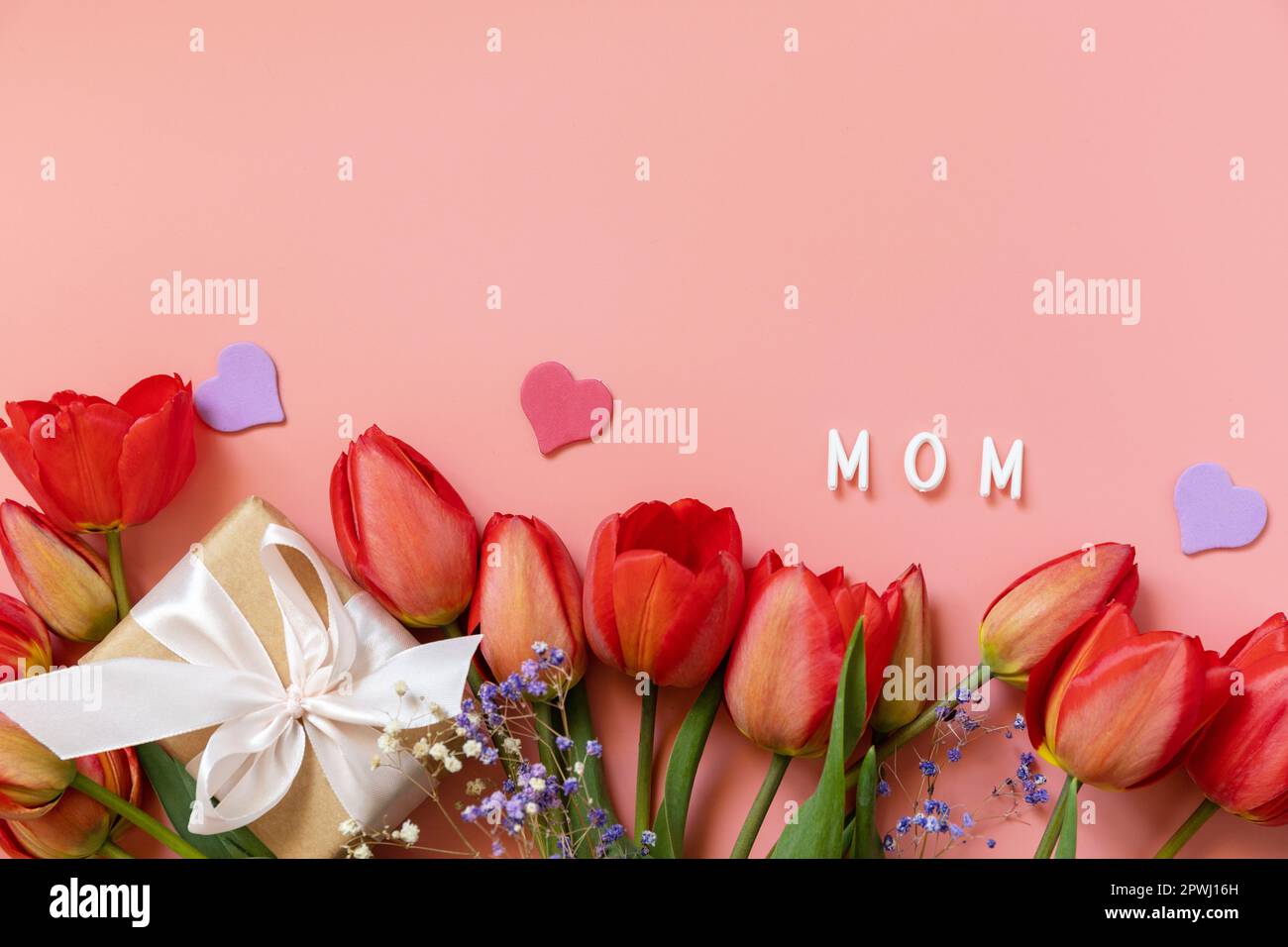 Geschenkbox mit Schleifen kleine Herzen und rote Tulpen auf pastellrosa Hintergrund mit leerem Platz. Muttertagsfeier-Konzept. Blick von oben. Stockfoto