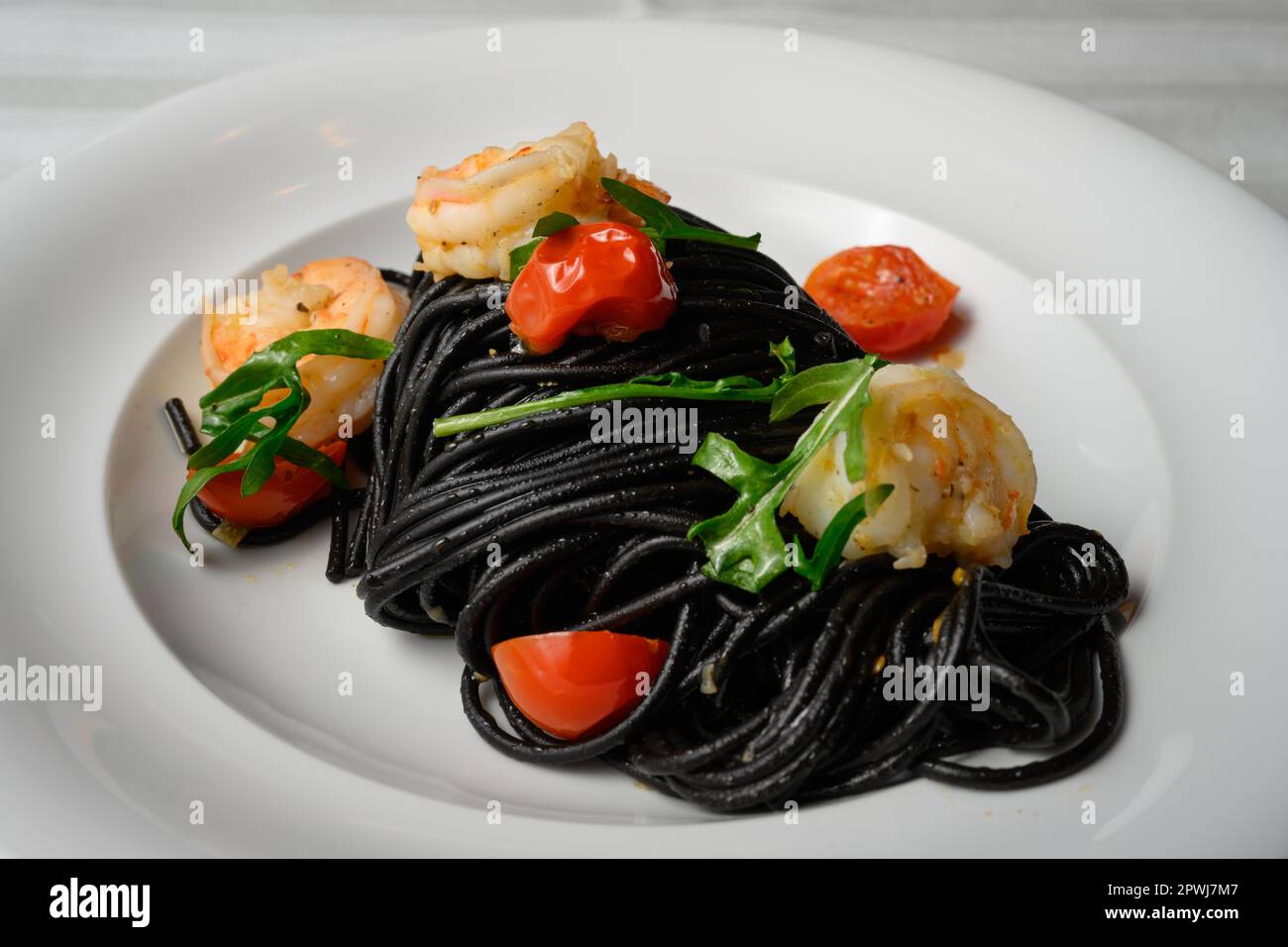 Spaghetti al Nero di Seppia con Gamberi, italienische Pasta mit Tintenfischtinte, Garnelen, Tomaten und Rucola Stockfoto