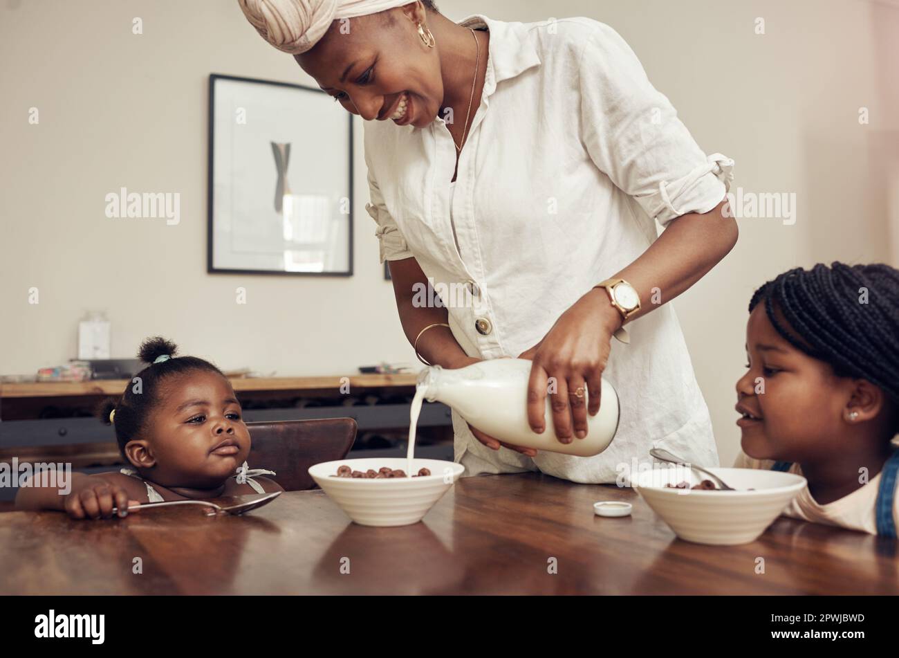 Beginnen Sie Ihren Morgen mit einer gesunden und leckeren Mahlzeit. Eine junge Mutter, die zu Hause Cornflakes für ihre beiden liebenswerten Töchter zubereitete Stockfoto