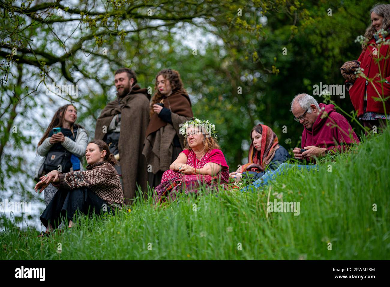 Die Menschen beobachten die Beltane-Zeremonie in Chalice Well, Glastonbury, Somerset, wo Beltane bei Sonnenaufgang und den ganzen Tag über gefeiert wird. Foto: Montag, 1. Mai 2023. Das Wort Beltane wird grob als „helles Feuer“ übersetzt und ist ein wichtiges Ritual, das heute als gälische Tradition überlebt, wo ein Beltane-Lagerfeuer angezündet wird. Als Reinigungs- und Heiler hätten die Menschen laufen, getanzt und über das Feuer gesprungen, während die Bauern ihre Rinder auch zwischen Lagerfeuer getrieben hätten, um sie zu reinigen und zu schützen, bevor sie auf die Felder gebracht wurden. Stockfoto