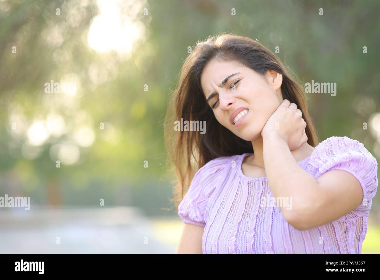 Gestresste Frau, die Nackenschmerzen hat, allein in einem Park Stockfoto