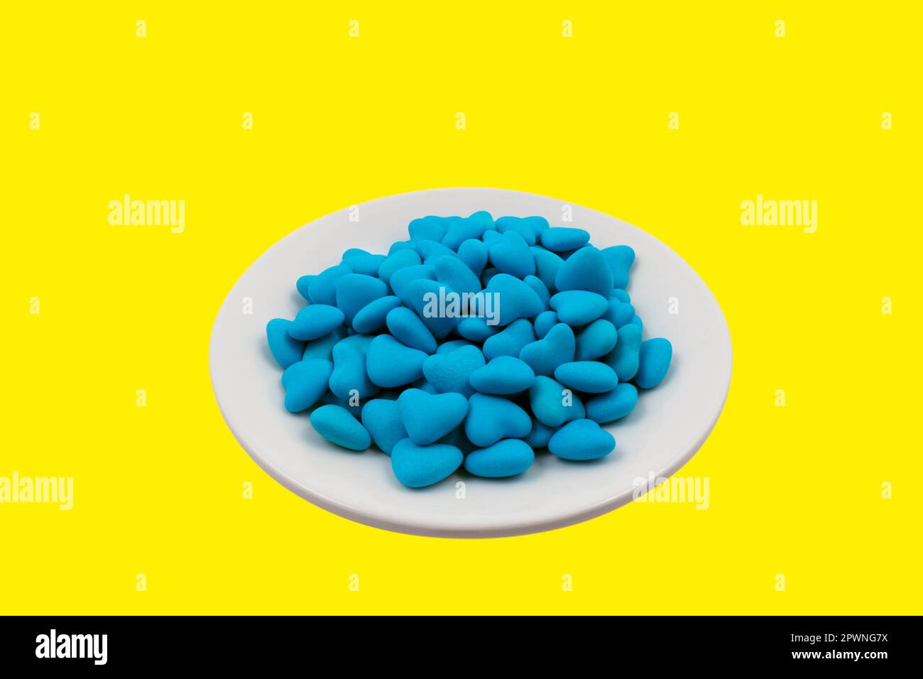 Weiße Platte mit blauen herzförmigen Süßigkeiten isoliert auf gelbem Hintergrund (nationale Symbole der Ukraine). Nahaufnahme, Draufsicht Stockfoto