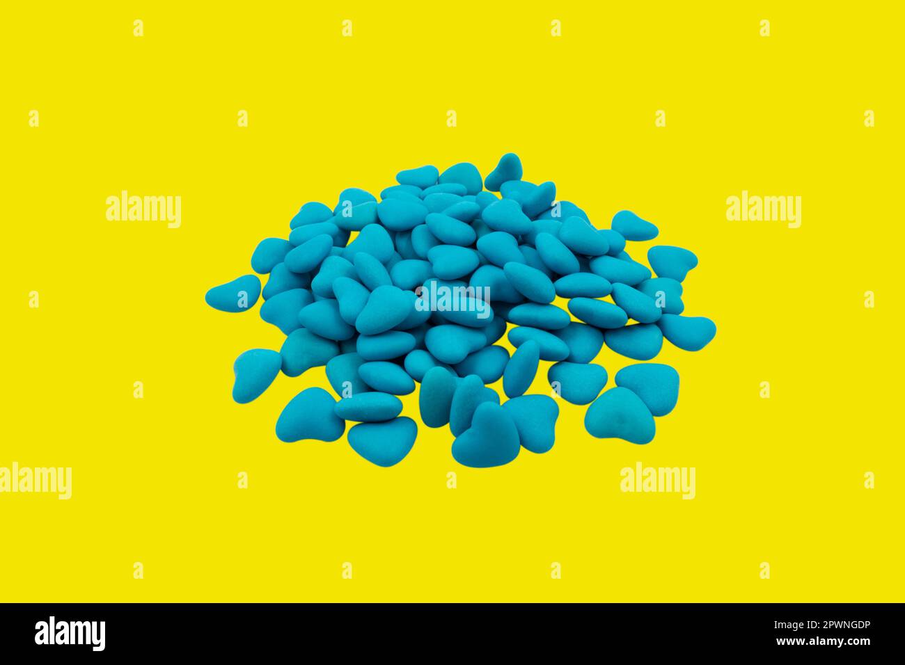 Ein Haufen blauer herzförmiger Süßigkeiten (Nahaufnahme), isoliert auf gelbem Hintergrund. Staatssymbole der Ukraine. Blick von oben Stockfoto