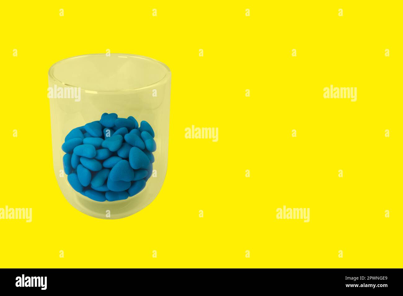 Glas mit blauen herzförmigen Süßigkeiten (Nahaufnahme) isoliert auf gelbem Hintergrund. Staatssymbole der Ukraine. Blick von oben Stockfoto