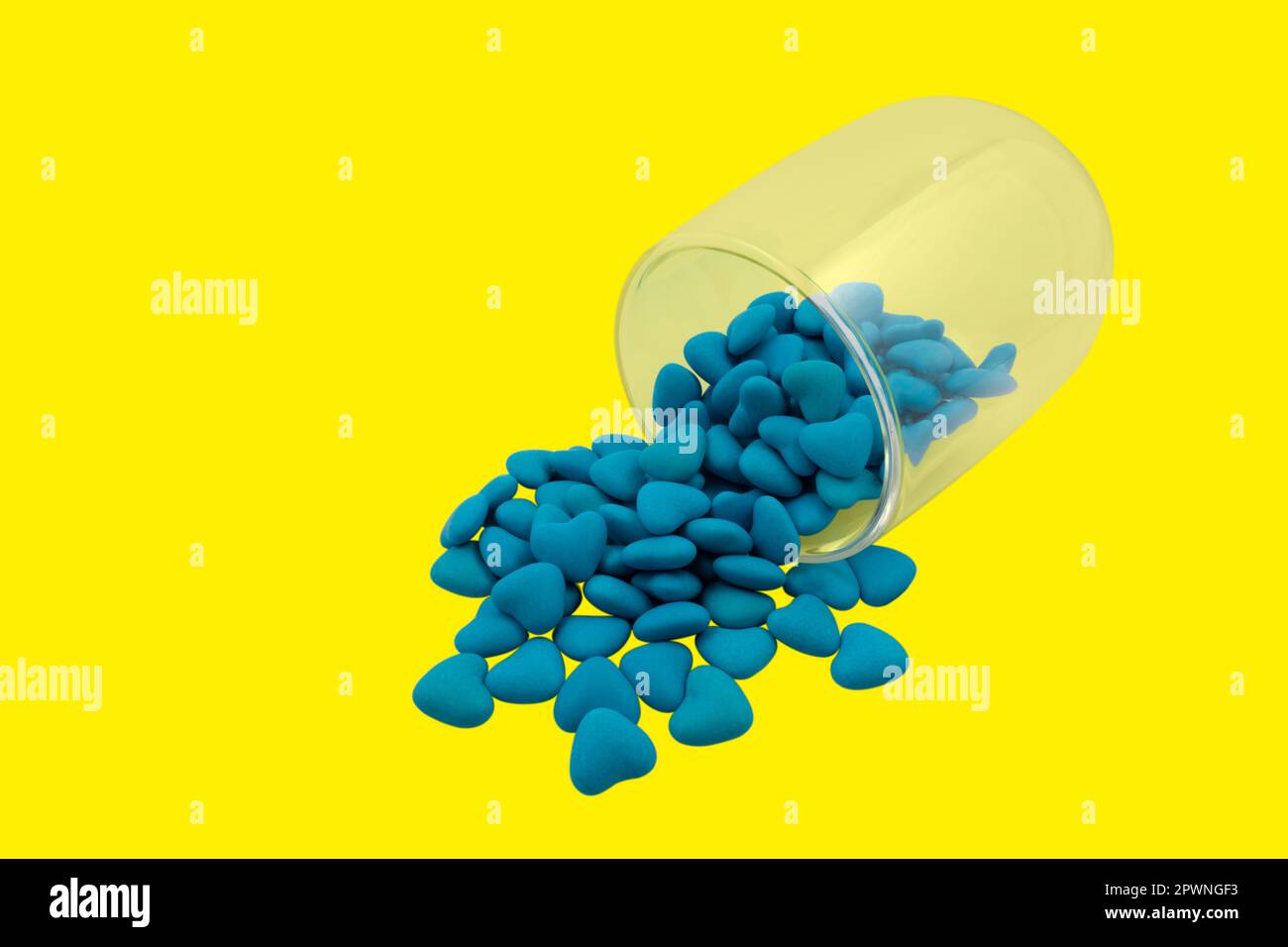 Umgedrehtes Glas mit blauen herzförmigen Süßigkeiten (Nahaufnahme), isoliert auf gelbem Hintergrund. Staatssymbole der Ukraine. Blick von oben Stockfoto