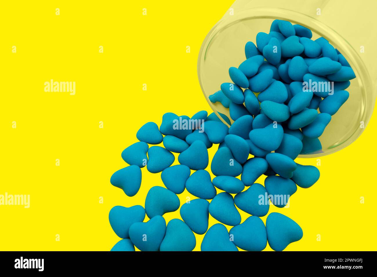 Umgedrehtes Glas mit blauen herzförmigen Süßigkeiten (Nahaufnahme), isoliert auf gelbem Hintergrund. Staatssymbole der Ukraine. Blick von oben Stockfoto