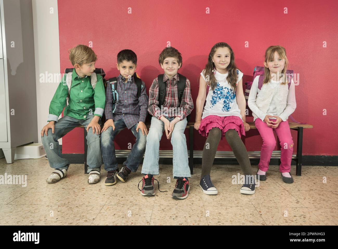Porträt von Schulkindern, die auf einer Bank im Korridor in Bayern sitzen Stockfoto