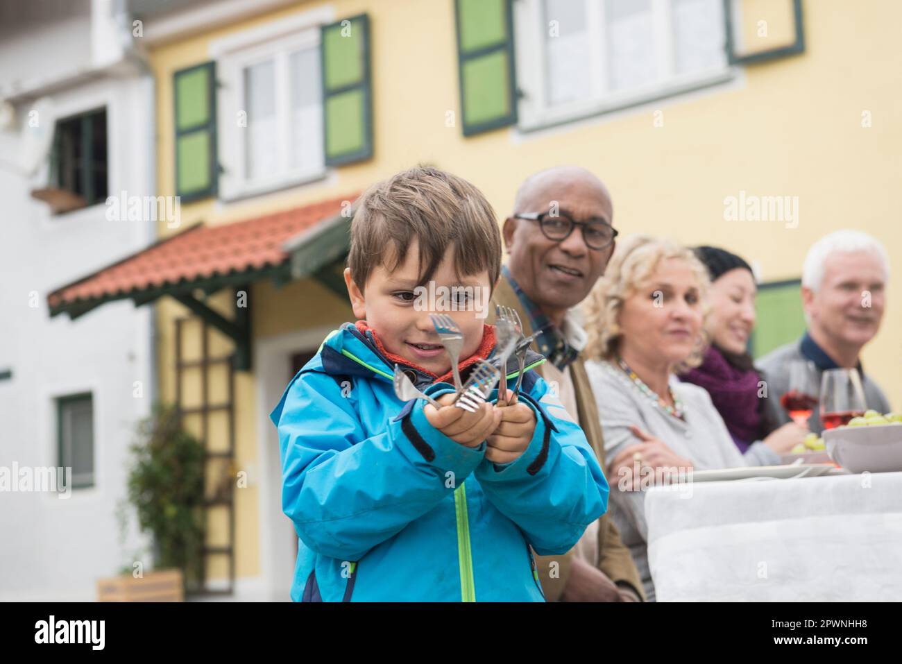 Ein kleiner Junge, der Gabeln in der Hand hält und seine Familie wartet auf ihn, Bayern, Deutschland Stockfoto