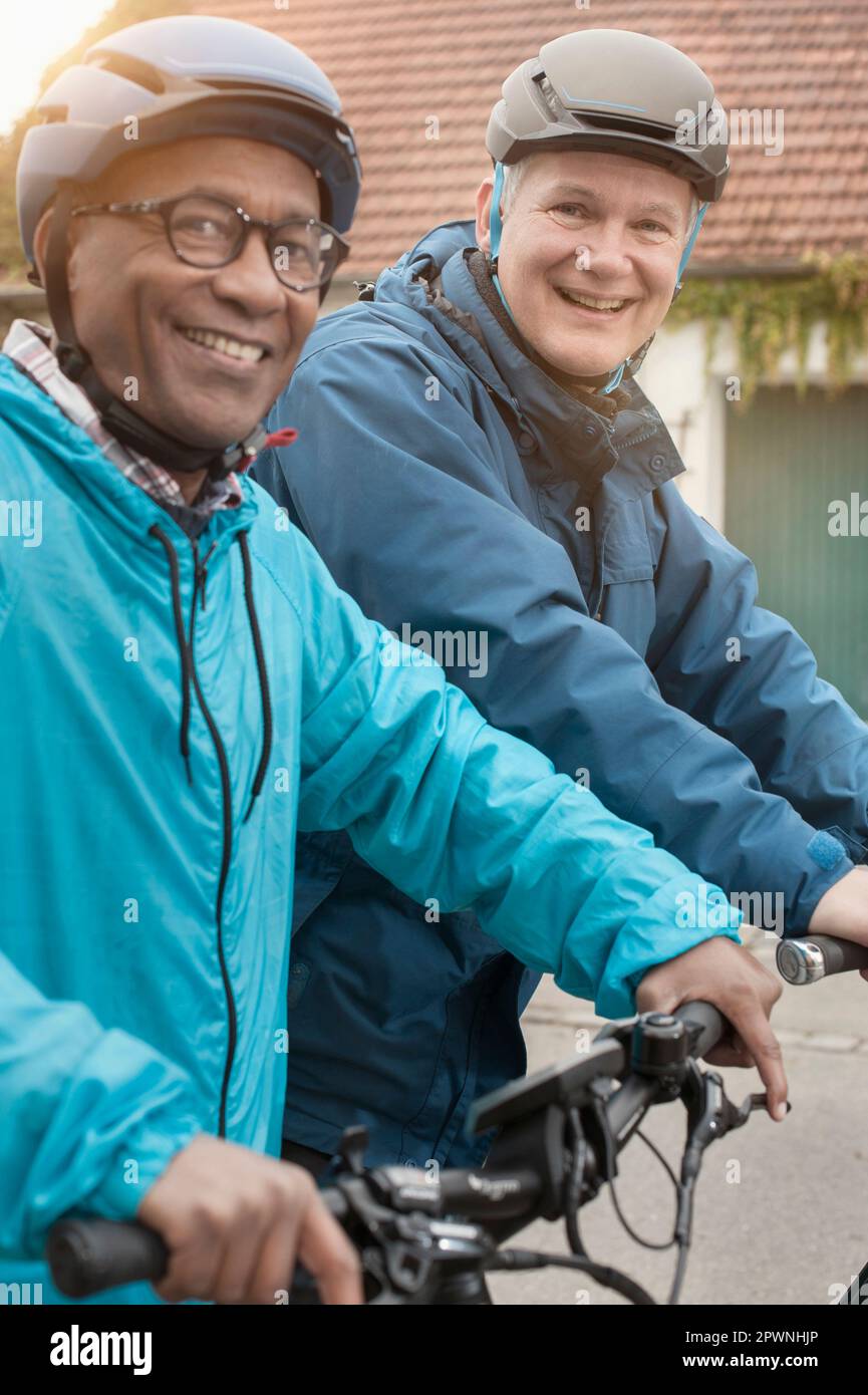 Männliche Freunde, die Rad fahren und lächeln auf der Straße, Bayern, Deutschland Stockfoto