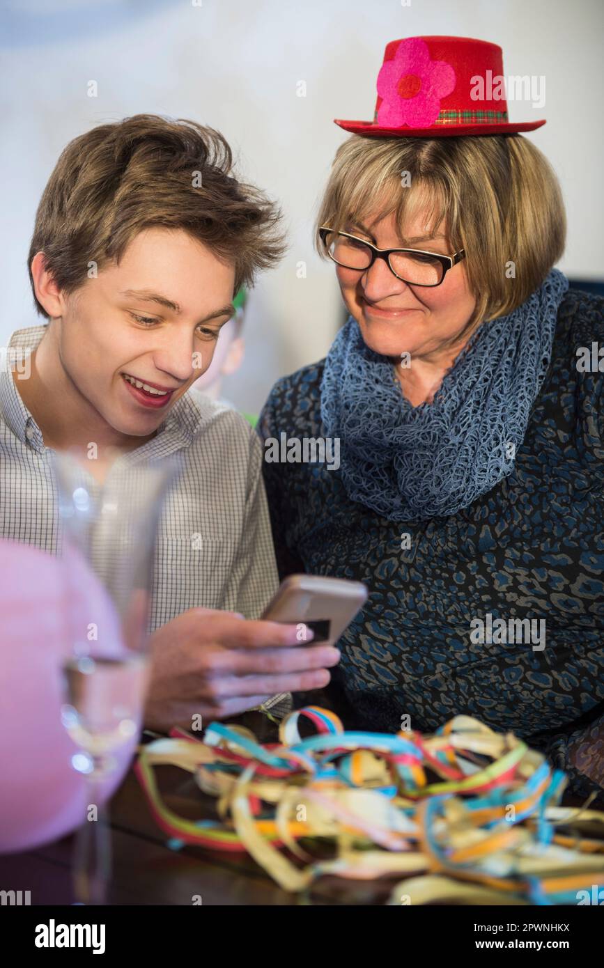 Teenager mit Großmutter, der auf einer Party ein Smartphone benutzt Stockfoto